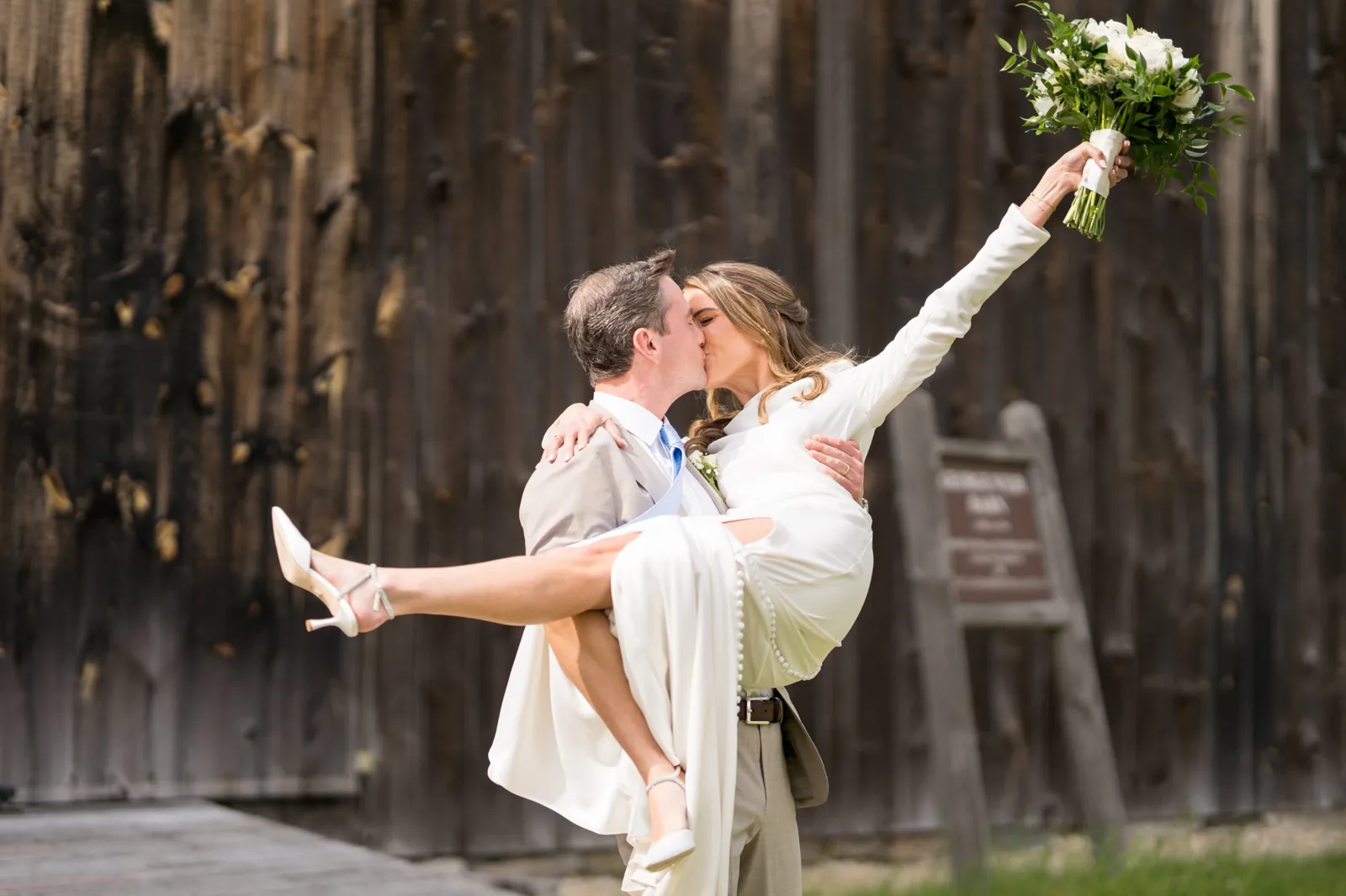 Groom lifts the bride for a kiss in front of a weathered barn, Long Island wedding photography