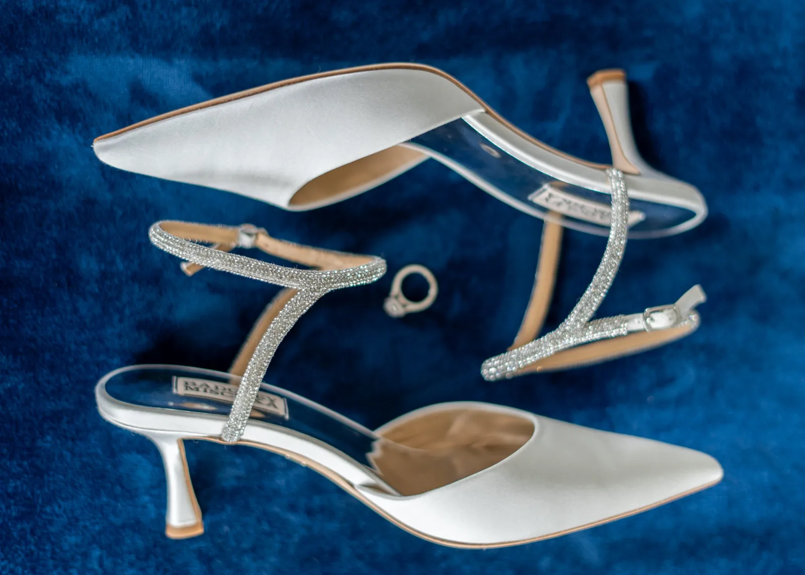 Crystal-strap bridal heels and wedding rings on blue velvet, wedding detail photography