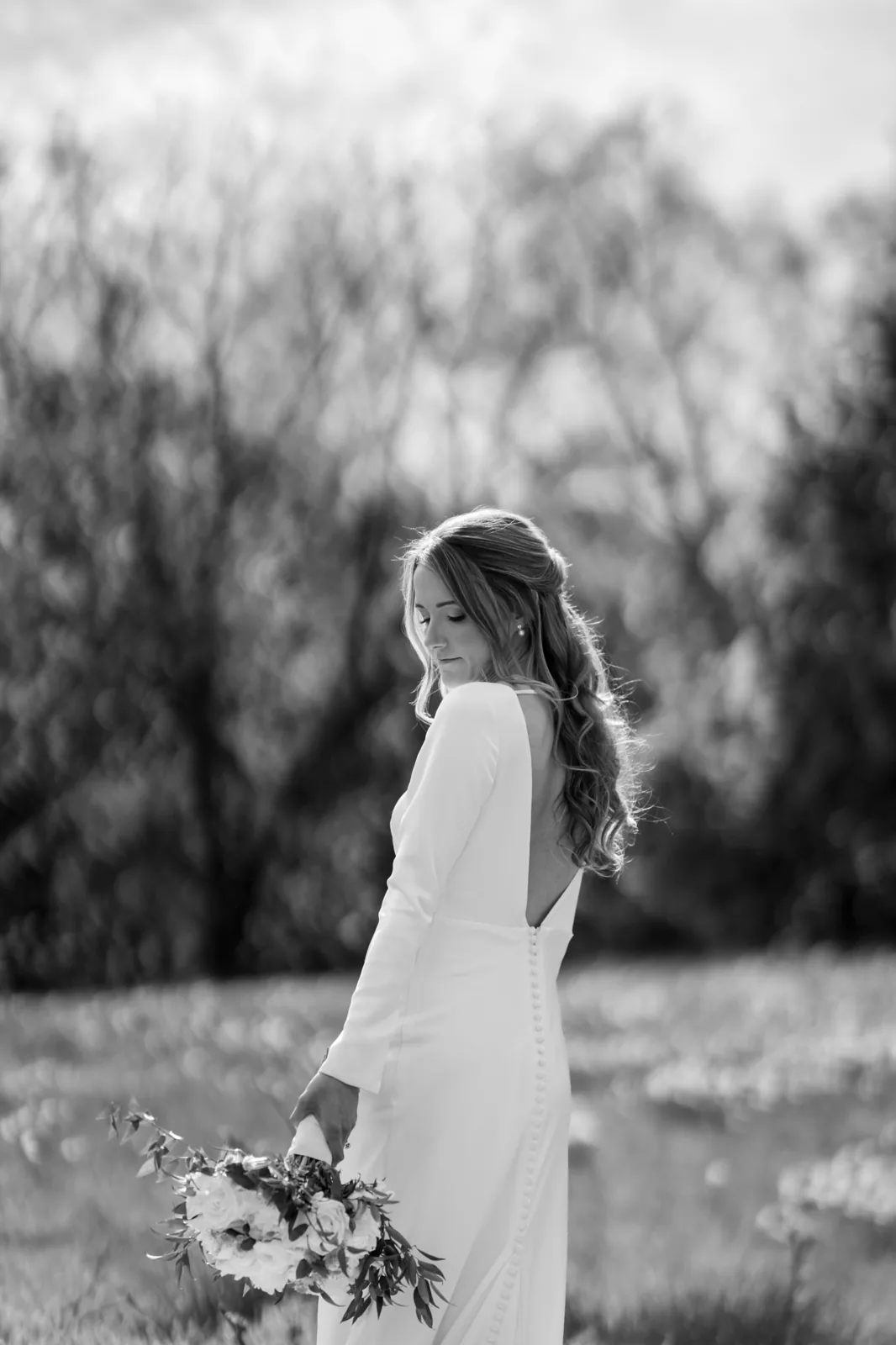 Black and white bridal portrait in a sunlit North Fork meadow, low-back long-sleeve gown