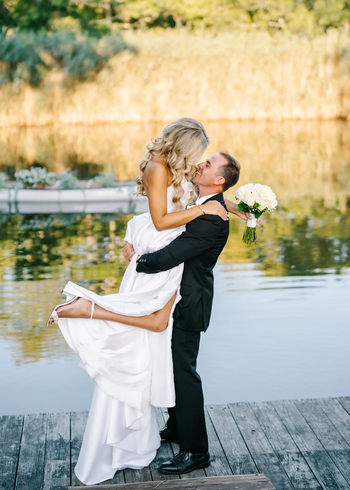 Groom lifts the bride on a dock at golden hour, waterfront Long Island wedding photography