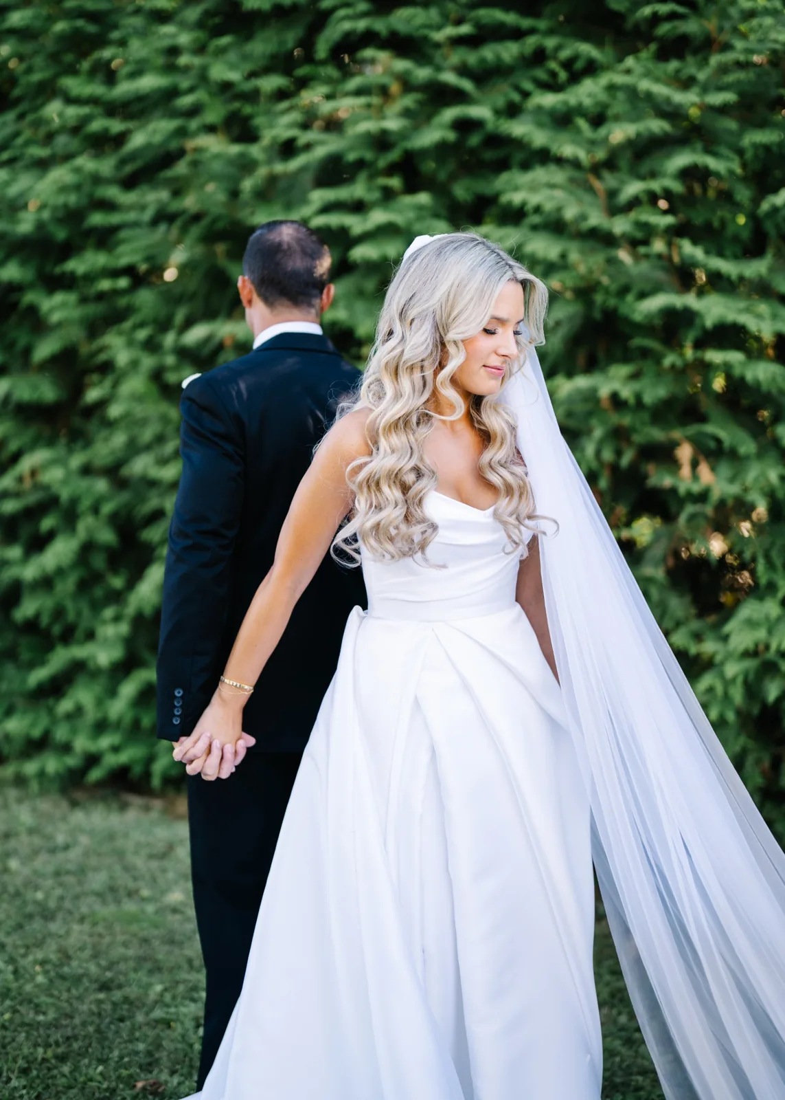 Bride and groom hold hands back to back for a first touch before the ceremony, cathedral veil, Long Island wedding