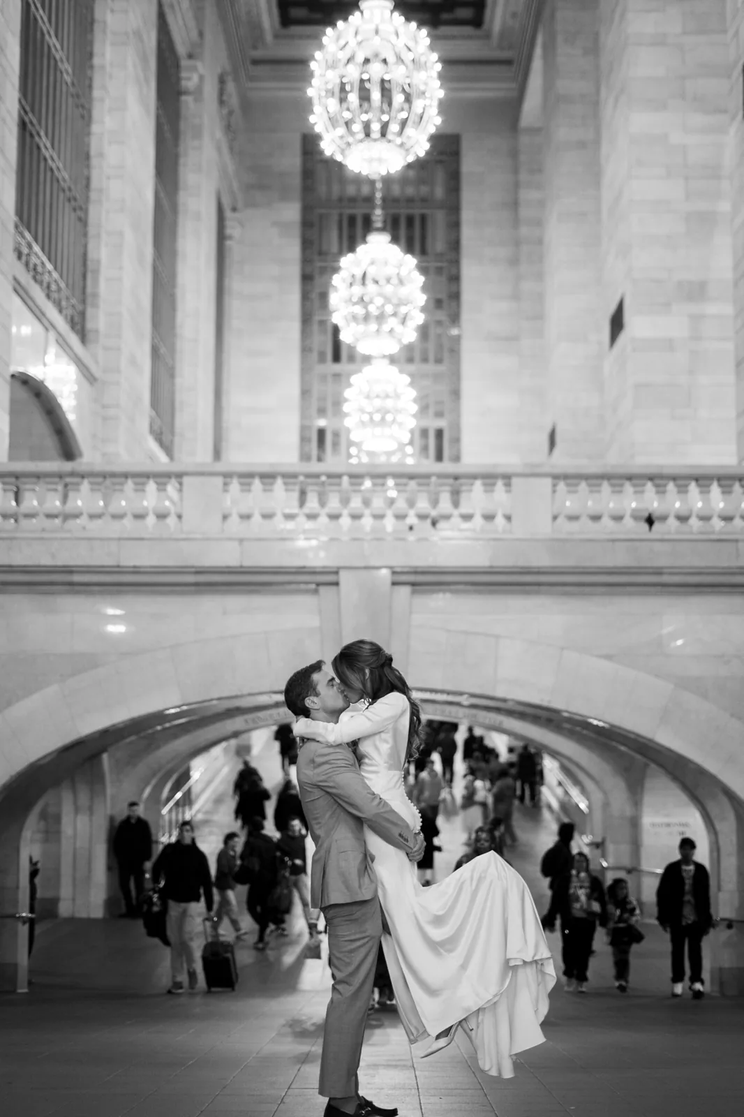 Groom lifts the bride for a kiss beneath the Grand Central chandeliers, black and white NYC wedding photo