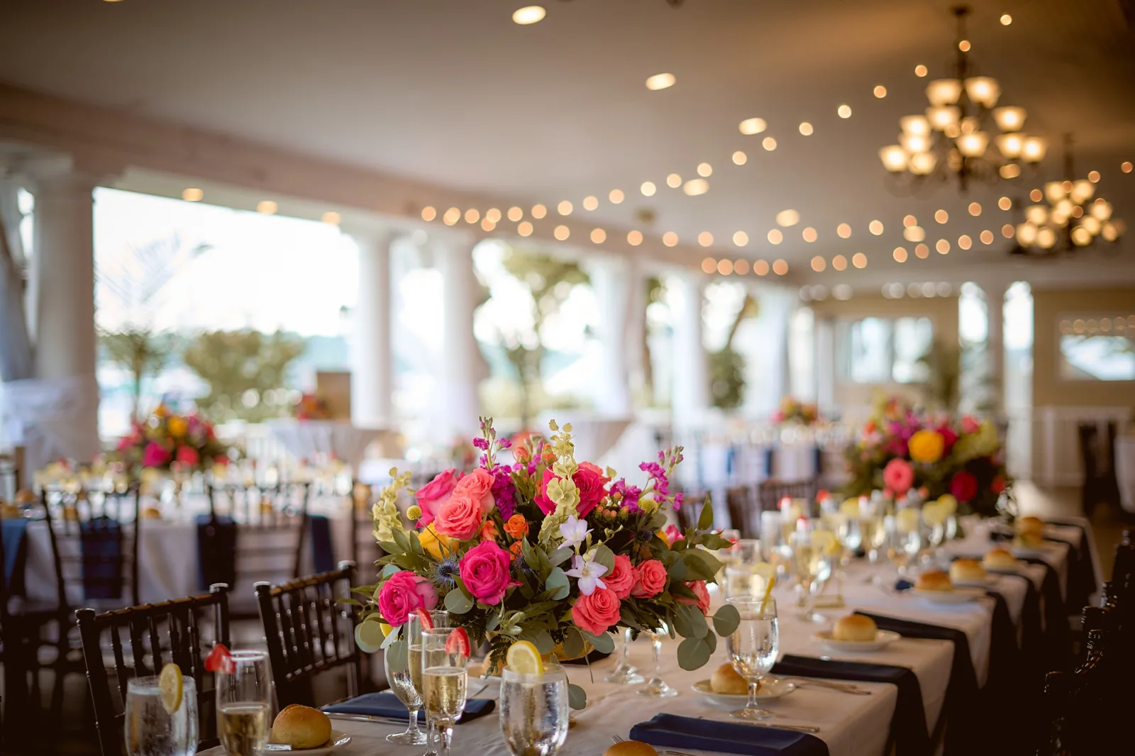 Reception tablescape with pink and coral florals under string lights, waterfront Long Island wedding venue