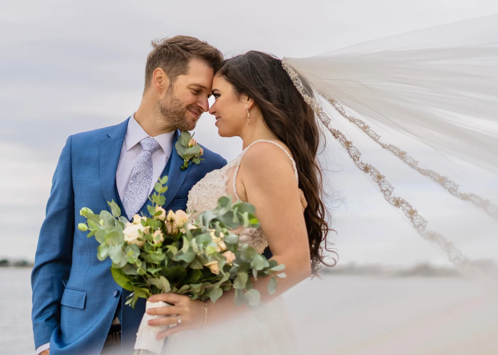 Bride and groom forehead to forehead as the veil catches the wind, Long Island waterfront wedding
